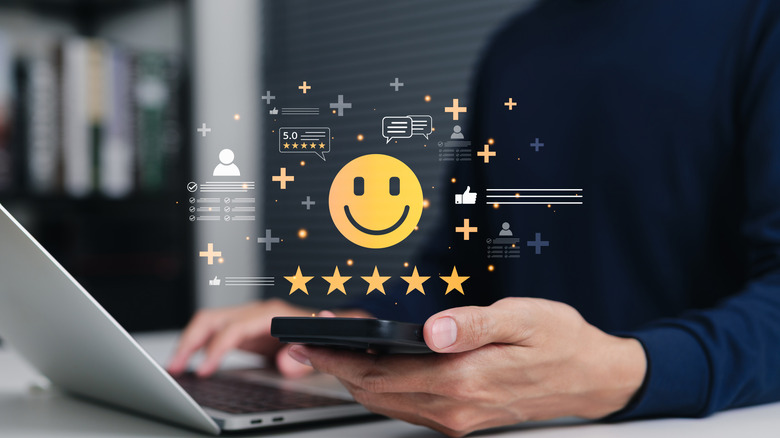 Holographic images of a happy emoji and five star ratings above a smartphone and a laptop.
