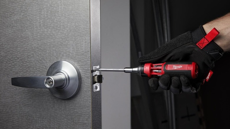 Using a multi-bit driver to work on a doorframe fastener.