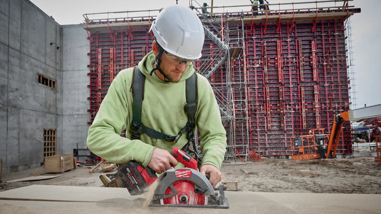 A circular saw being used to cut wood by someone in safety equipment.