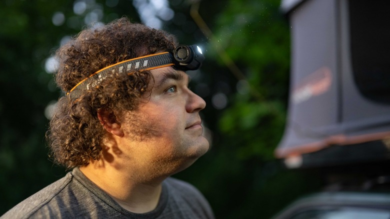 Andy Zahn wearing the powered-on Fenix HM70R Headlamp, standing next to a rooftop tent at twilight.