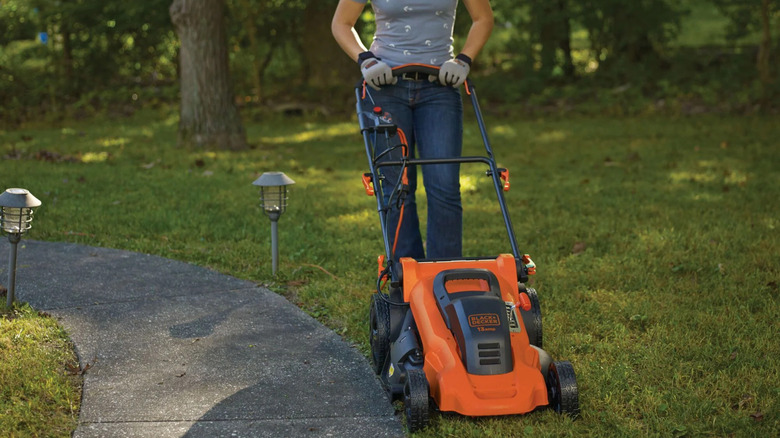 A oerson pushing an orange lawn mower close to a curved pathway