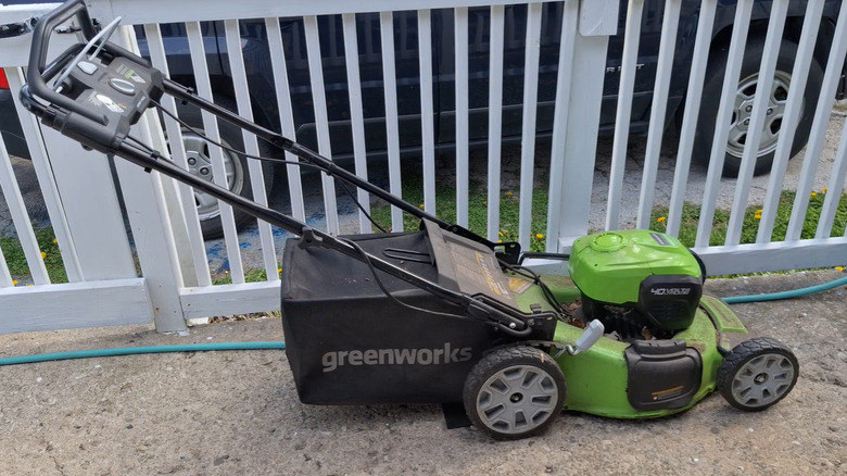 A Greenworks lawn mower parked beside a white fence