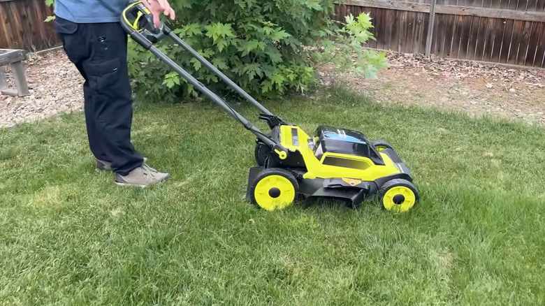 A person navigating a lawn mower across a patch of tall grass