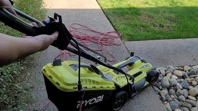 A person starting a corded Ryobi lawn mower