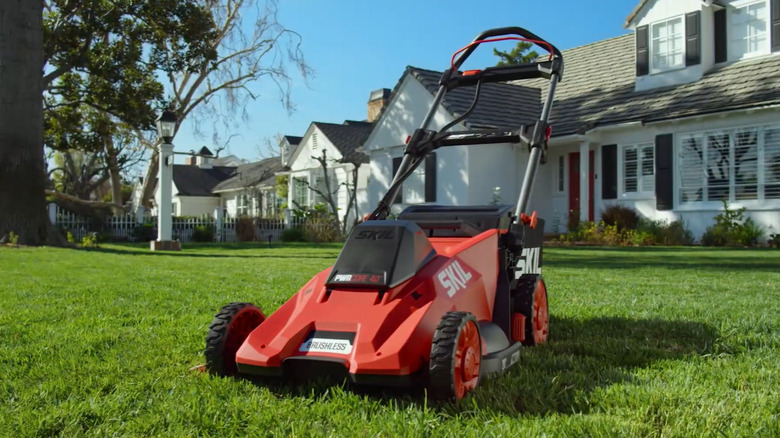 A SKIL lawn mower with a row of houses in the background