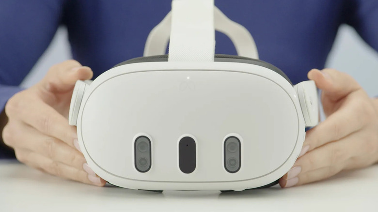 A person holding the Meta Quest 3 headset in both hands on a white surface
