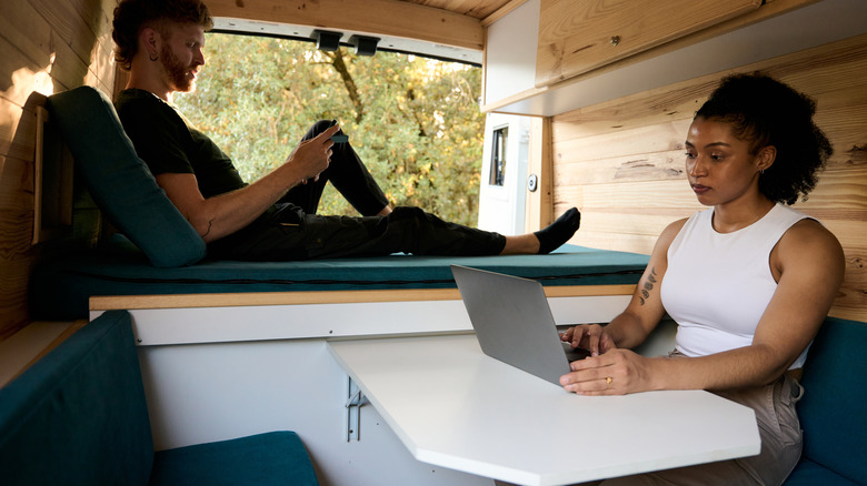 Two people in a van, one working and the other on their phone.
