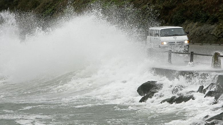 A wave hitting a bridge as a van drives over it.