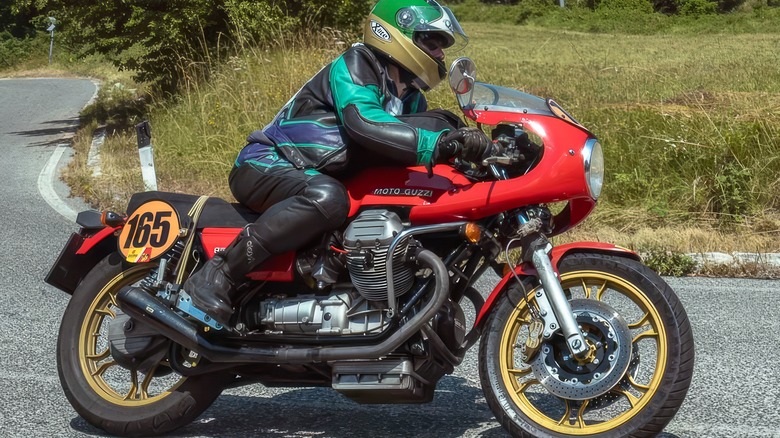 Rider cornering on a classic red Moto Guzzi Le Mans, outfitted with racing fairings and number plate 165.