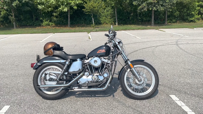 A 1977 Harley-Davidson XLH Sportster 1000 parked in an empty lot, featuring a custom black tank and retro helmet.