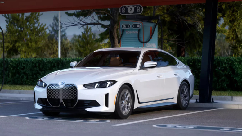 A white BMW i4 Gran Coupe fastback sedan standing at a charging station in the shade.