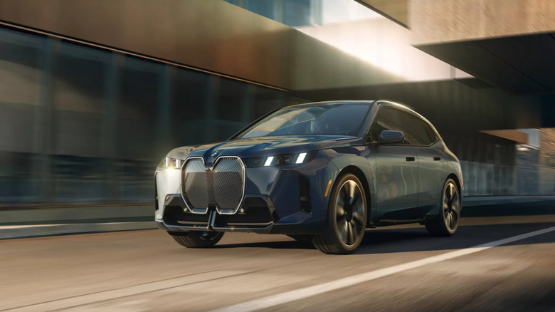 A blue BMW iX for the final 2026 model year (in the US) on a freeway, moving underneath an underpass.