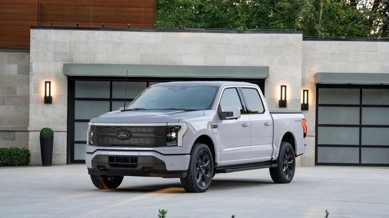 A gray 2025 Ford F-150 Lightning all-electric pickup truck standing in front of a modern home garage door.