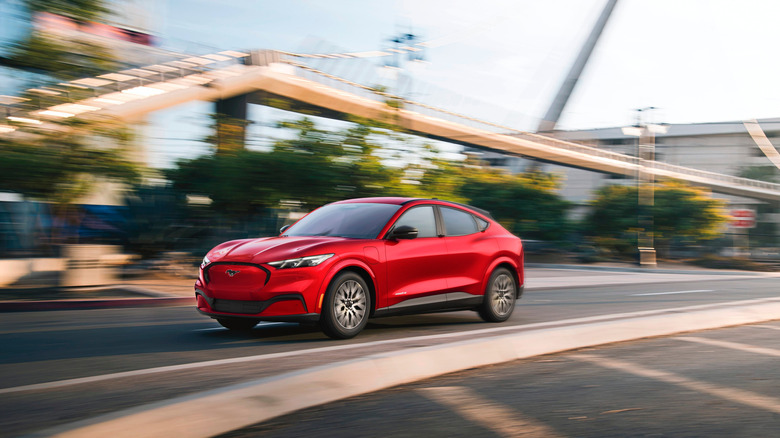 A red 2026 Ford Mustang Mach-E crossover SUV moving at speed down a road, with the background blurred.