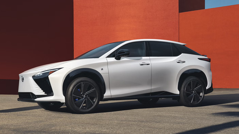 A white Lexus RZ for 2026 parked in front of a modern-looking red building in the background.