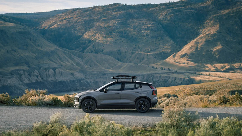 A Vapor Gray 2026 Volvo EX30 compact SUV standing at the side of a road, with a river and mountains in the back.