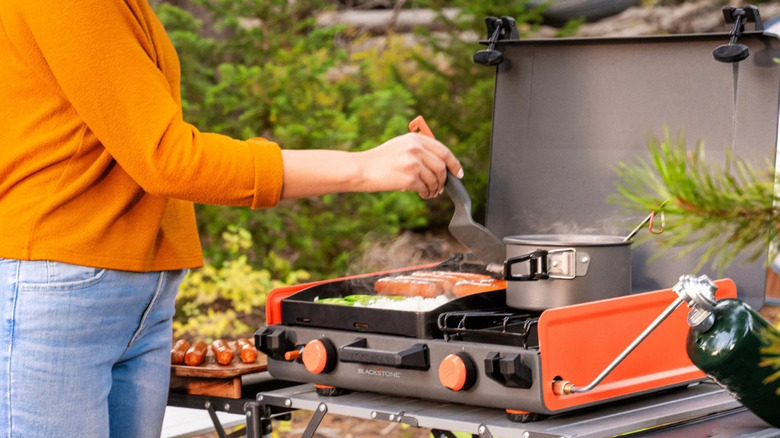 A person cooking outdoors on the Blackstone Camping Griddle and Side Burner