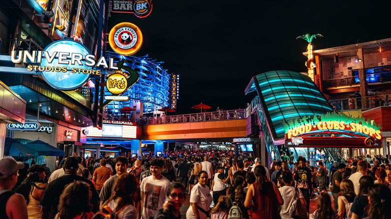 A citywalk with a large crowd, there are many stores' logos over them.