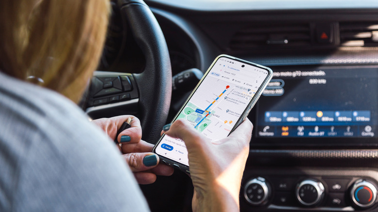 A picture of a woman holding a smartphone displaying directions on Google Maps in her car.