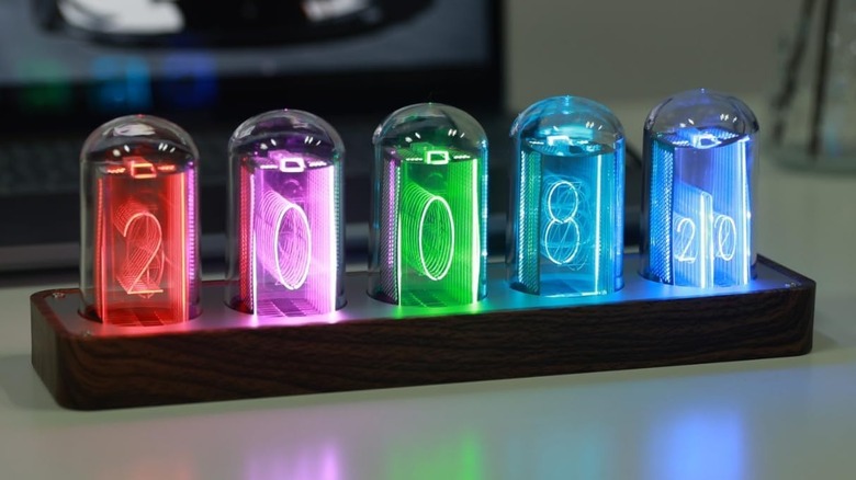 The ClocTeck Nixie Tube Clock with multiple colors for each number, placed on a white desk in front of a laptop