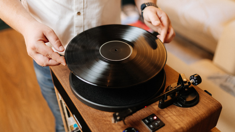 A person placing a vinyl record on a wooden turntable