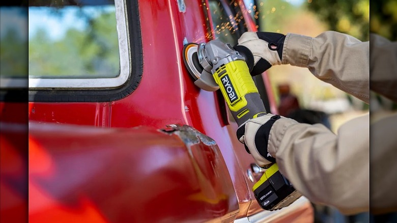 Using angle grinder to work on a red vehicle.