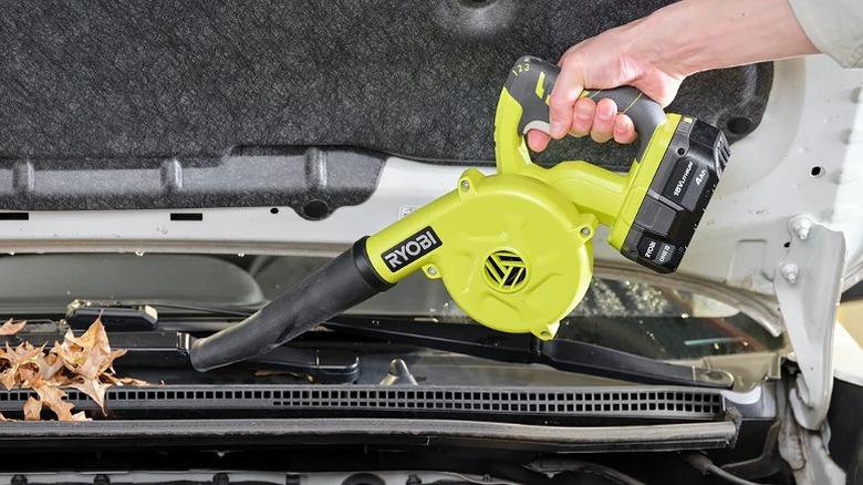 Using workshop blower to clear leaves from a car's windshield.
