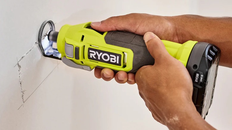 A worker cutting piece out of drywall with Ryobi cut-out tool