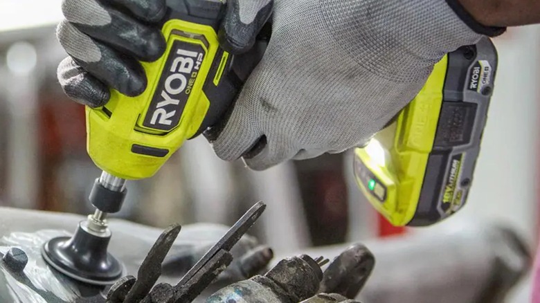 A worker wearing gloves grinding away material with Ryobi die grinder