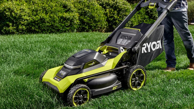 A landscaper cutting grass with a Ryobi lawn mower