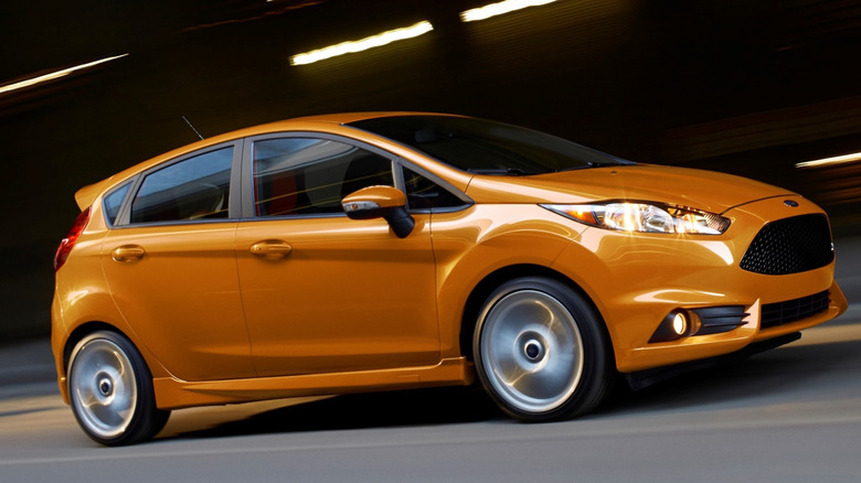 An orange Ford Fiesta ST moving at speed down a road with the background blurred due to the speed.