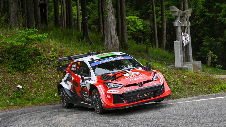 A Toyota GR Yaris with racing sponsor sticker on it taking a curve down a narrow road at speed.