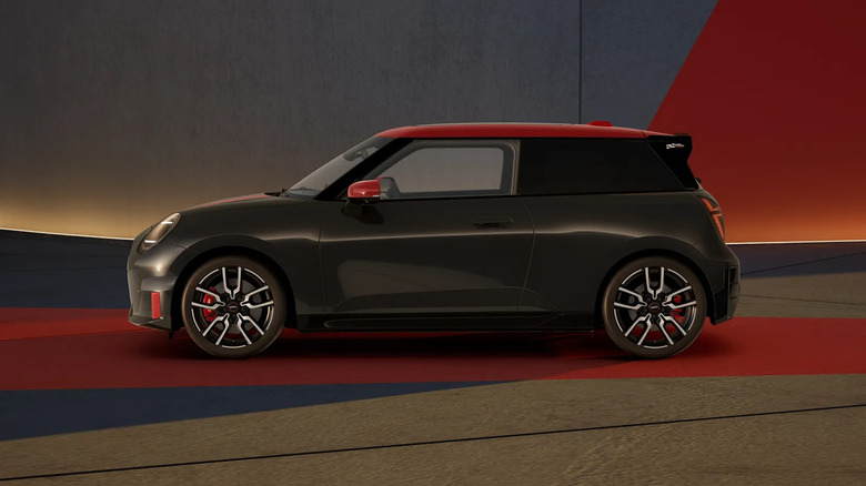 A red and black 2026 Mini Cooper John Cooper Works car parked in front of a wall, side view visible.