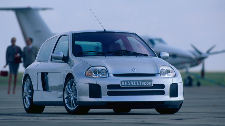 A silver Renault Clio V6 car standing, parked at an angle on a road on an overcast day.