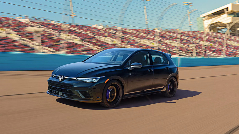 A blue Volkswagen Golf R zooming down a racetrack while blurred spectators look on in the background.