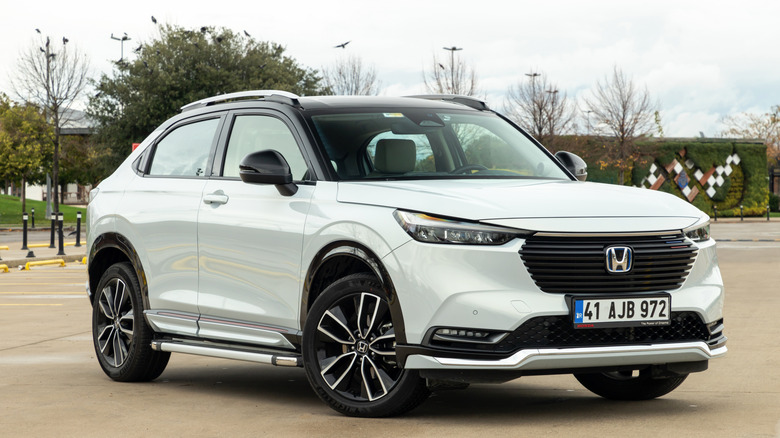 A white 2022 Honda HR-V mini-SUV standing isolated in a parking lot, front-right view photographed.
