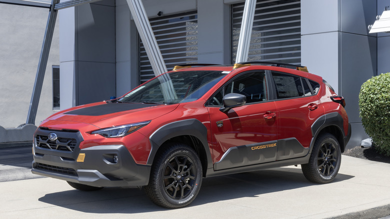 A red and black 2024 Subaru Crosstrek parked outside a modern gray building in the afternoon.