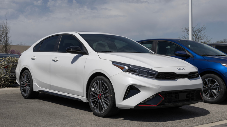 A white 2024 Kia Forte GT parked outside in the open in a dealer lot in the afternoon.