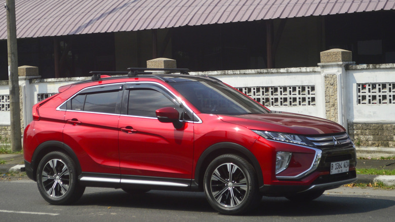 A red Mitsubishi Eclipse Cross SUV passing through a busy street, photographed left to right.