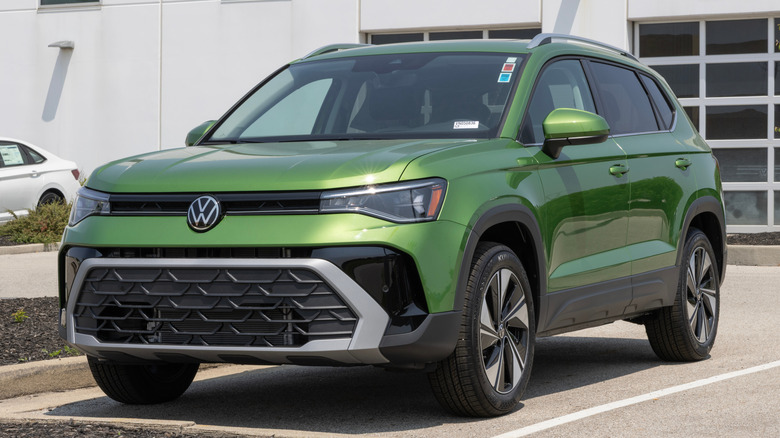 A green 2025 Volkswagen Taos parked within the white lines of a parking bay outside in the open.