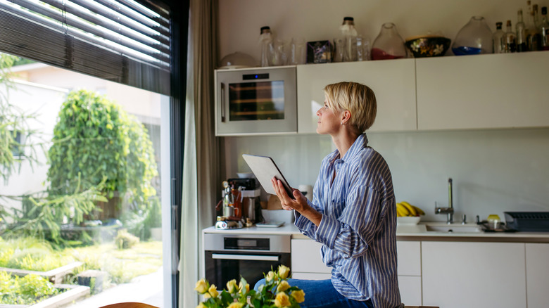 Woman using a tablet to open or close window blinds