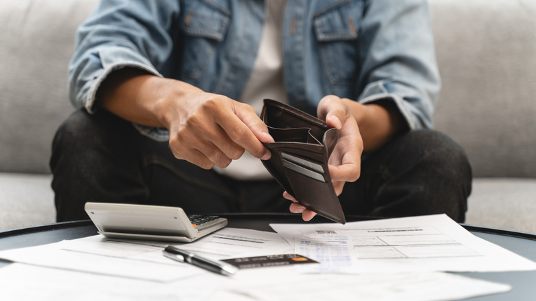 A man with an empty wallet doing his finances on a table with papers and a calculator