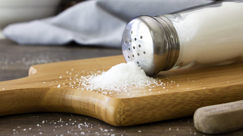 A knocked over salt shaker on a cutting board with a pile of salt