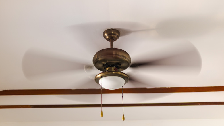 Ceiling fan on a white ceiling, spinning so that the blades appear blurry