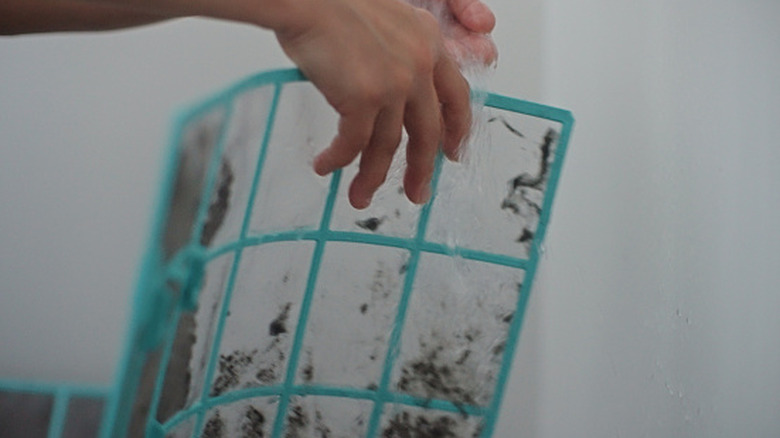 Hand holding and rinsing a visibly dirty air conditioner filter