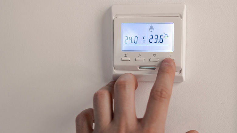 A hand making adjustments to a wall-mounted thermostat