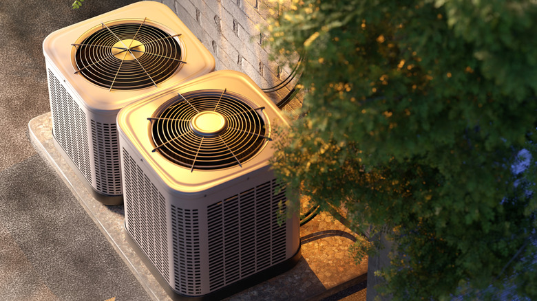 Two air conditioner units outside a building with greenery above them