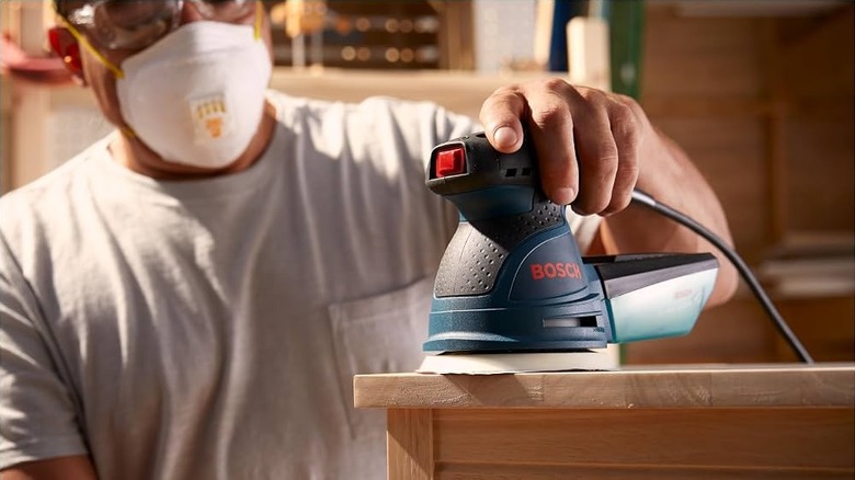 A person using the Bosch Palm Variable Speed Random Orbit Sander on a wooden table