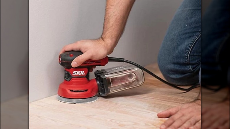Worker sanding hardwood floor with Skil sander