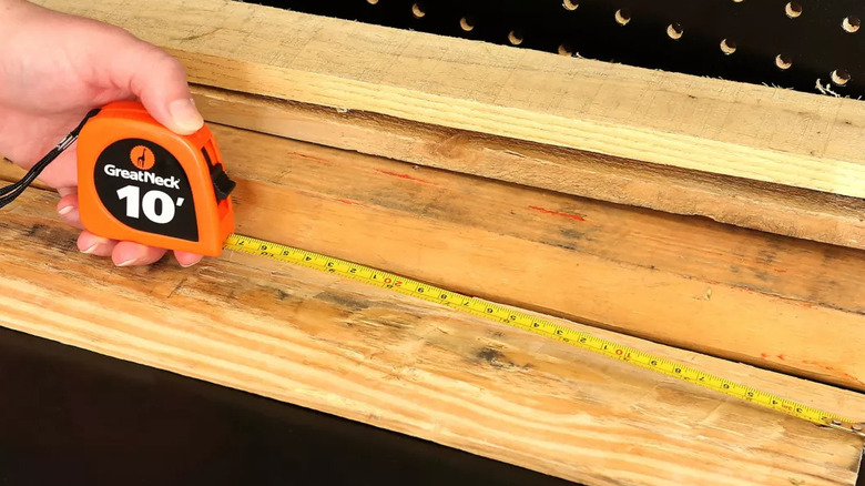 Hand holding a GreatNeck measuring tape measuring a piece of wood